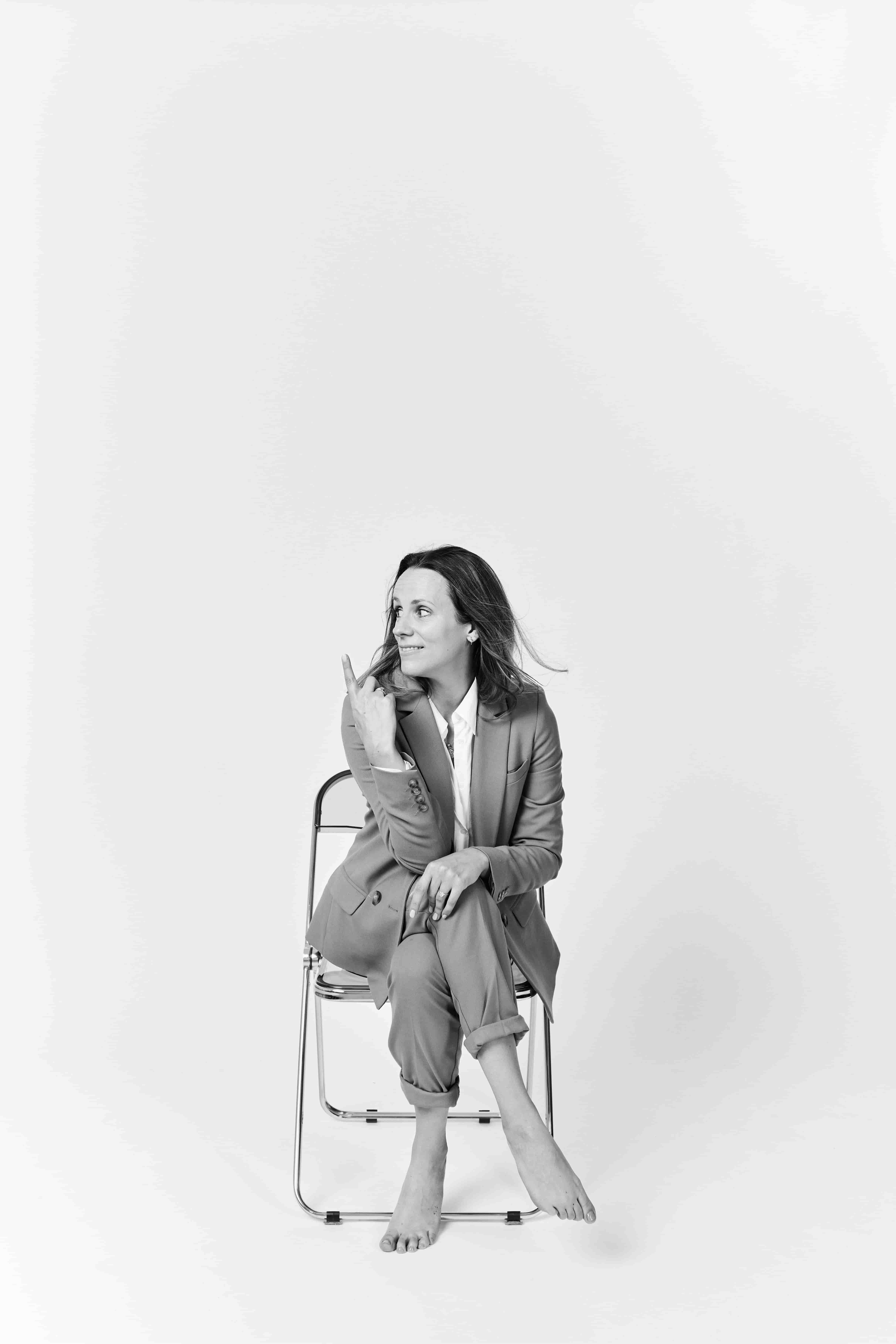 Chloe seated on a folding chair, looking away and pointing upward
